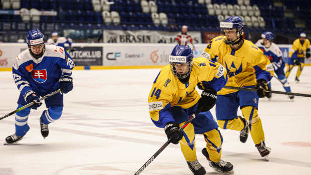 A hockey player in a yellow jersey competes in a game with a teammate not far behind him.